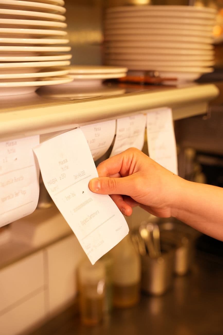 A hand pulling order tickets in a busy kitchen